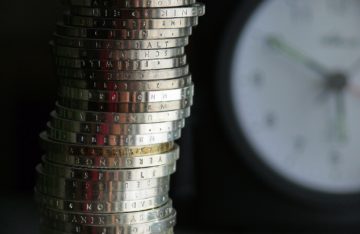 Euromünzen gestapelt vor dem Hintergrund einer verschwommenen Uhr