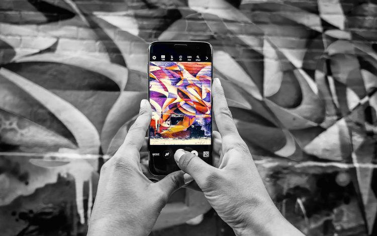 Smartphone wird vor bunte Graffiti Wand gehalten, sodass Streetart online animiert wird